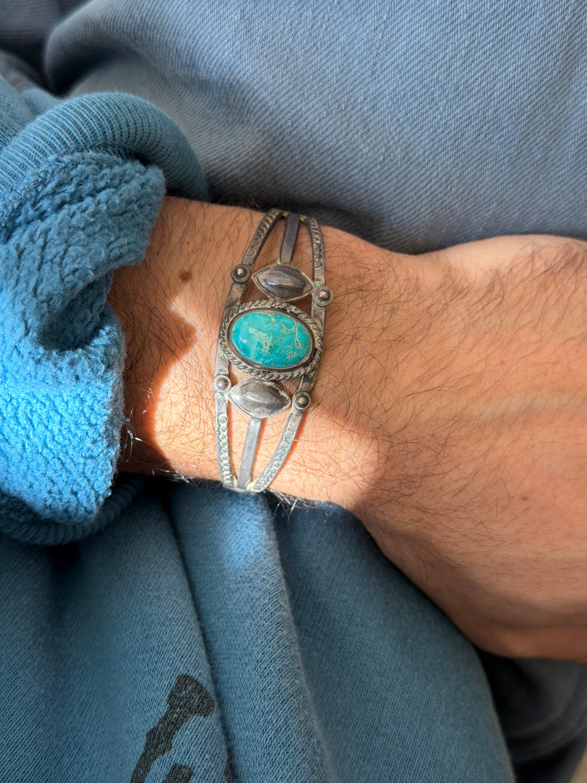 Sterling silver triple band cuff with an oval turquoise cabochon in a twisted rope bezel, flanked by domed leaf shapes, on the wrist