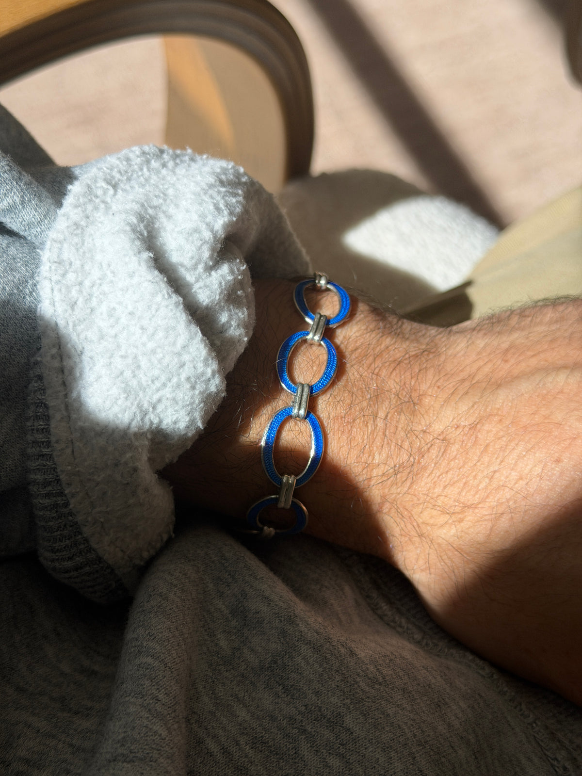 Blue enamel oval link bracelet on the wrist, sunlight showing the engine turned texture beneath the translucent cobalt enamel
