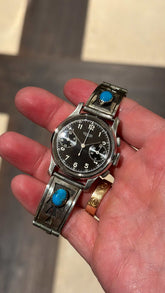 Vintage 1940s Heuer 32mm baby chronograph watch with black dial and turquoise sterling silver bracelet held in hand from Collectors Gene