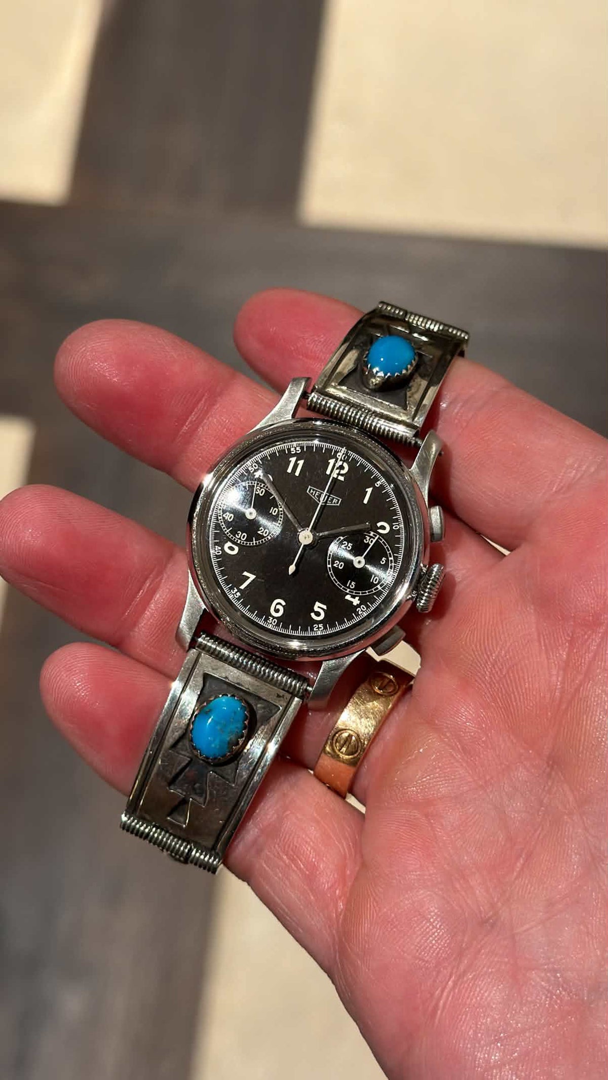 Vintage 1940s Heuer 32mm baby chronograph watch with black dial and turquoise sterling silver bracelet held in hand from Collectors Gene