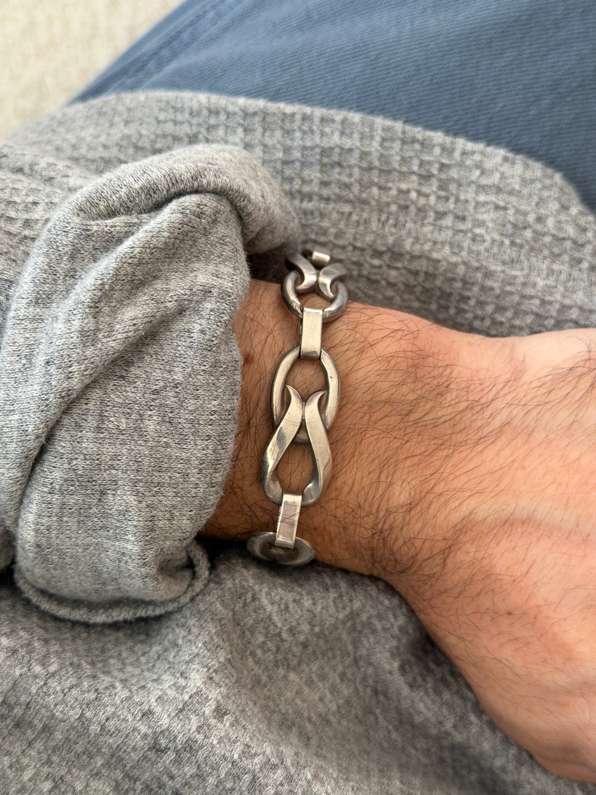 Mid century sterling silver bracelet of twisted figure eight links joined by flat bars, worn on the wrist against a gray knit sleeve