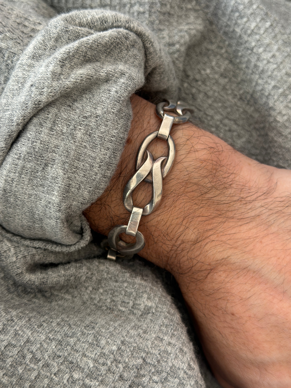 Close wrist view of the twisted link bracelet, a folded silver ribbon loop through an oval ring with smooth bar connectors