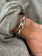 Close wrist view of the twisted link bracelet, a folded silver ribbon loop through an oval ring with smooth bar connectors