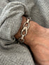 Close wrist view of the twisted link bracelet, a folded silver ribbon loop through an oval ring with smooth bar connectors
