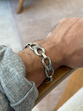 Twisted silver link bracelet on the wrist resting on a wooden chair arm, the bold sculptural links catching the light