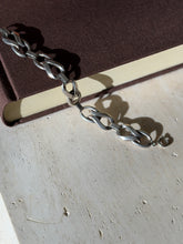 Sterling twisted link bracelet draped from a brown book onto travertine, ending in a spring ring clasp