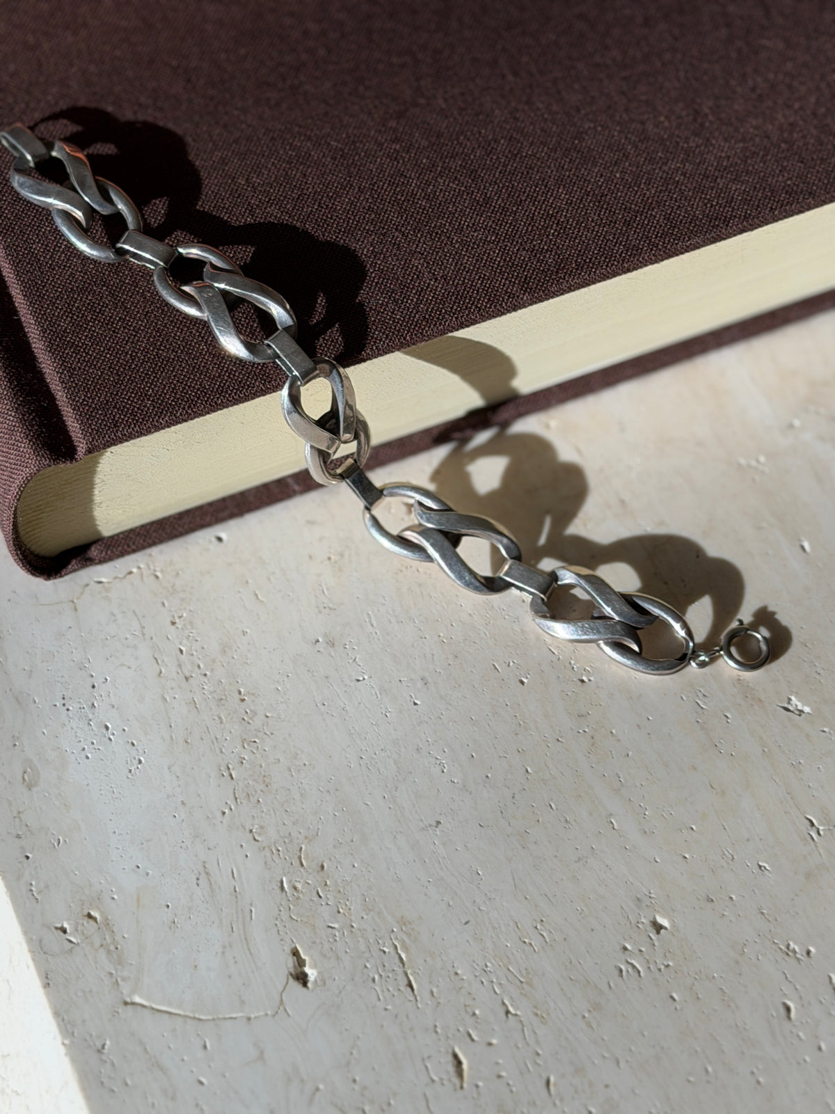 Sterling twisted link bracelet draped from a brown book onto travertine, ending in a spring ring clasp