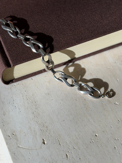 Sterling twisted link bracelet draped from a brown book onto travertine, ending in a spring ring clasp