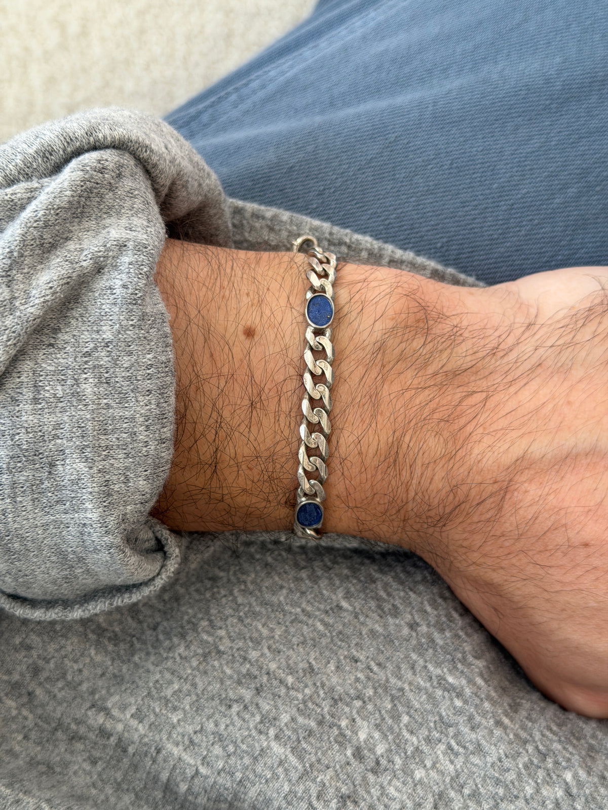 Wrist view of the lapis curb bracelet over blue denim, deep blue stones flecked with gold pyrite set flush in silver bezels