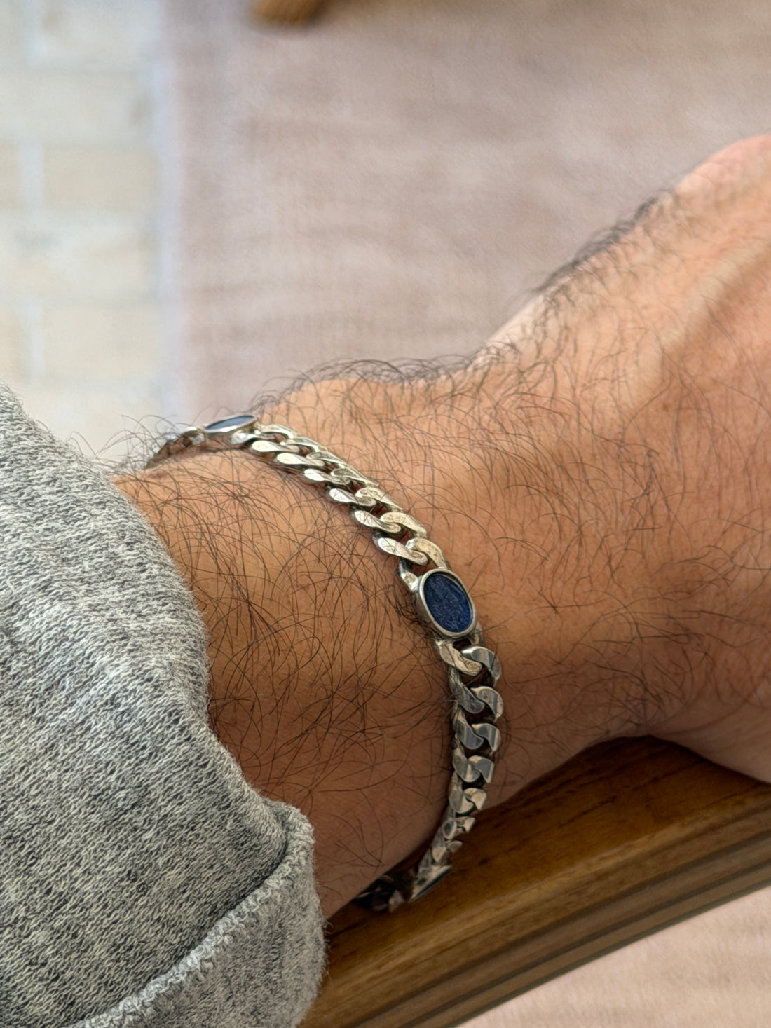 Close side view of the sterling and lapis bracelet on the wrist resting on a wooden chair arm, the faceted curb links catching the light