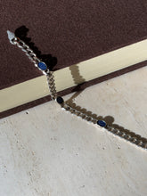 Lapis lazuli curb bracelet draped from a brown book onto travertine in raking sunlight, its box clasp at one end