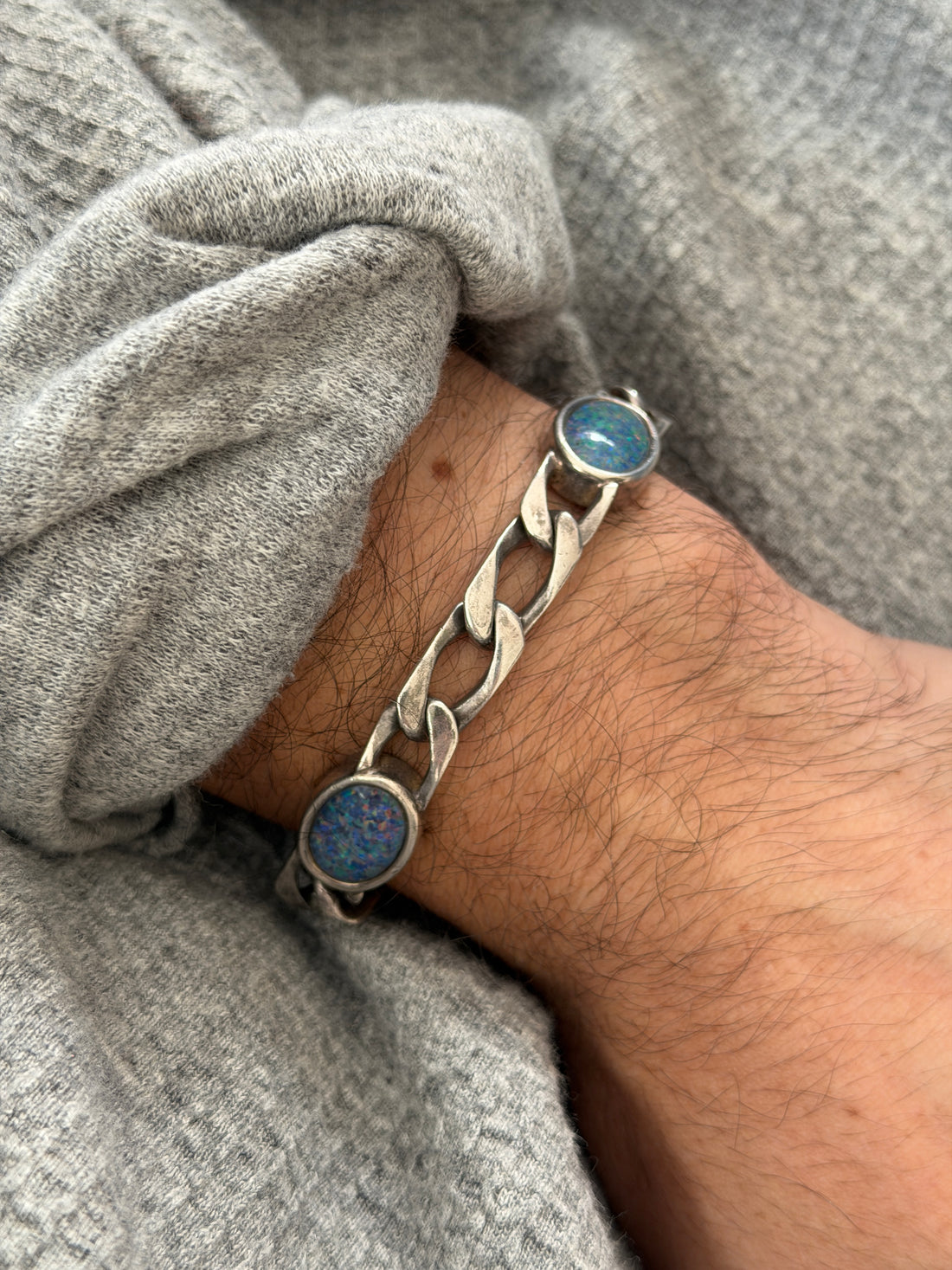 Angled wrist view of the opal and silver bracelet, flecks of blue and green fire in the round bezel set stones