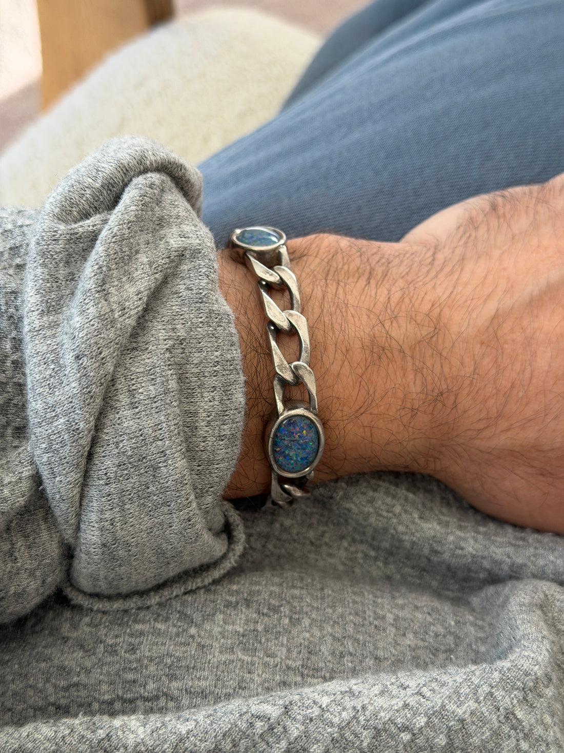 Side wrist view of the sterling opal bracelet, an oval cabochon with sparkling blue fire beside chunky patinated links