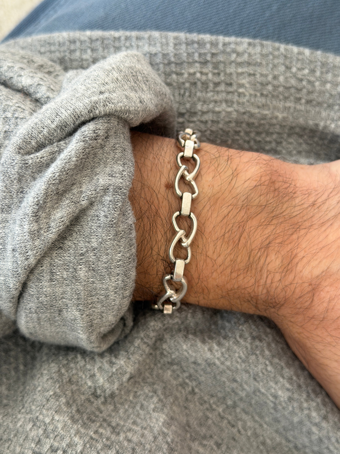 Vintage German sterling silver bracelet of open heart shaped oval links and flat bar connectors, worn on the wrist over a gray sweater