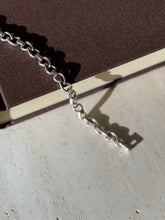 Sterling oval link bracelet draped over a brown book edge onto travertine, showing the box clasp and bar connectors in raking light