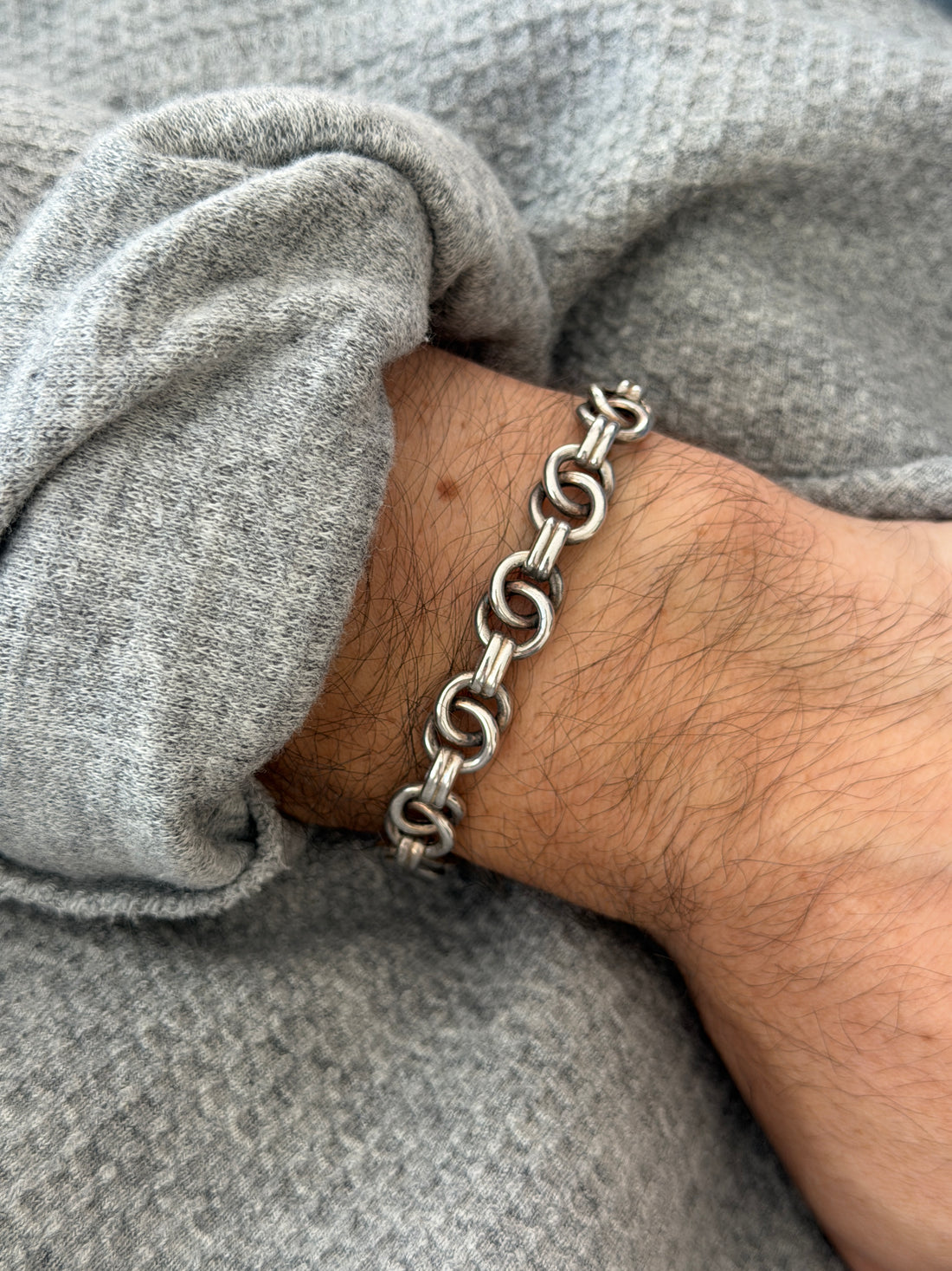 Angled wrist view of the ring link bracelet, pairs of polished silver rings joined by ribbed connectors over a gray sweater