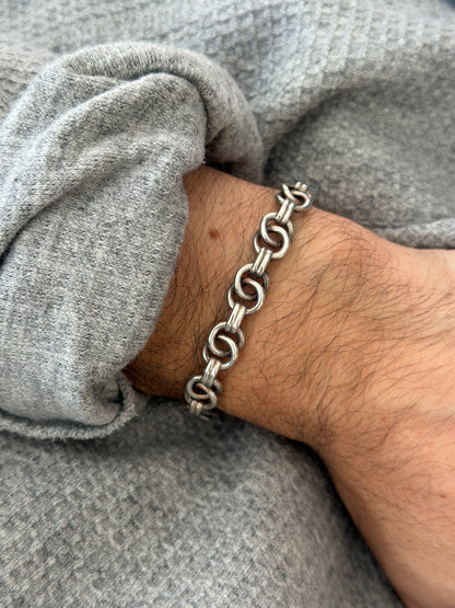 Angled wrist view of the ring link bracelet, pairs of polished silver rings joined by ribbed connectors over a gray sweater