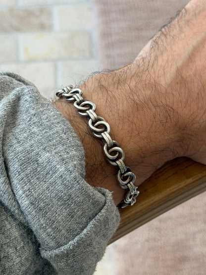 Close side view of the sterling ring link bracelet on the wrist resting on a wooden chair arm, darker patina in the recesses