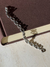 Ring link silver bracelet draped from a brown book onto travertine, its spring ring clasp and looping shadows in sunlight