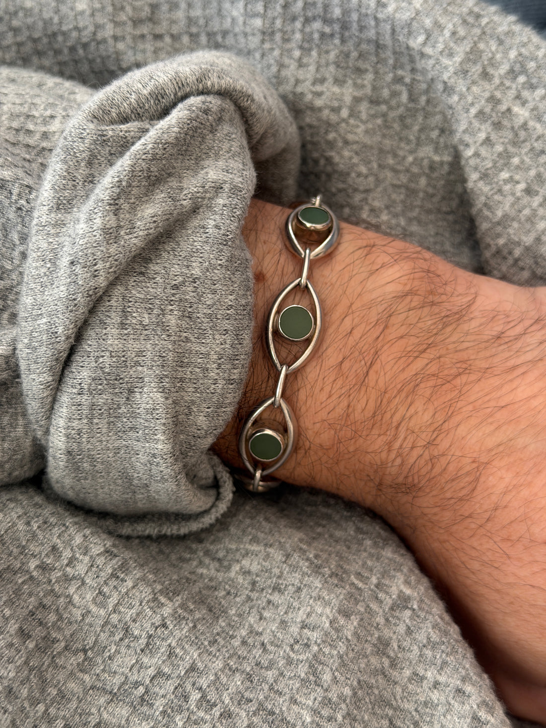 Close wrist view of the jade eye link bracelet, smooth bezel set green discs floating inside polished silver almond frames