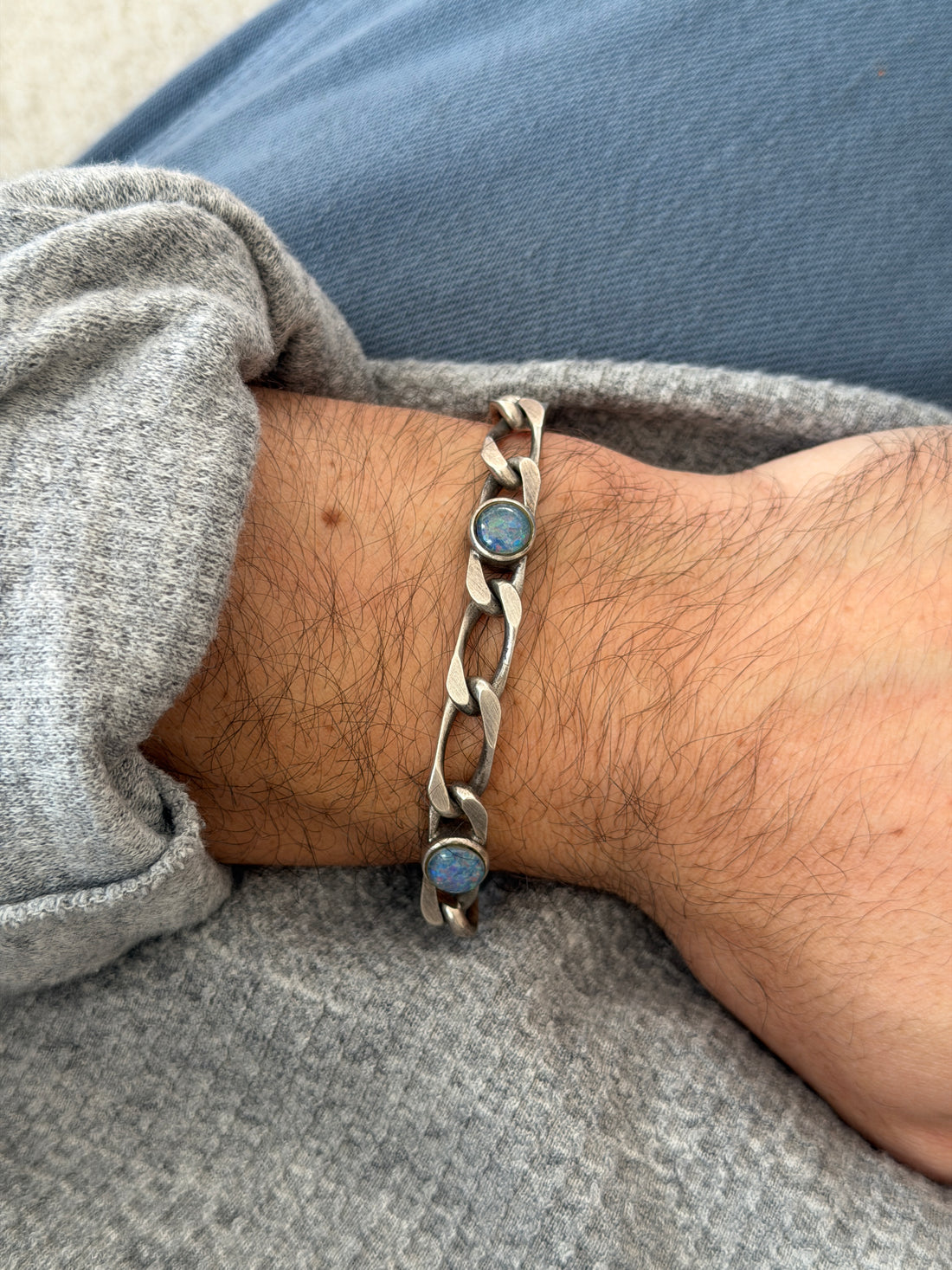 Vintage German sterling silver bracelet of long and short figaro style links set with round opal cabochons, worn on the wrist over a gray sweater