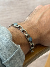 Opal and silver link bracelet on the wrist resting on a wooden chair arm, the brushed elongated links and two glowing opals in focus