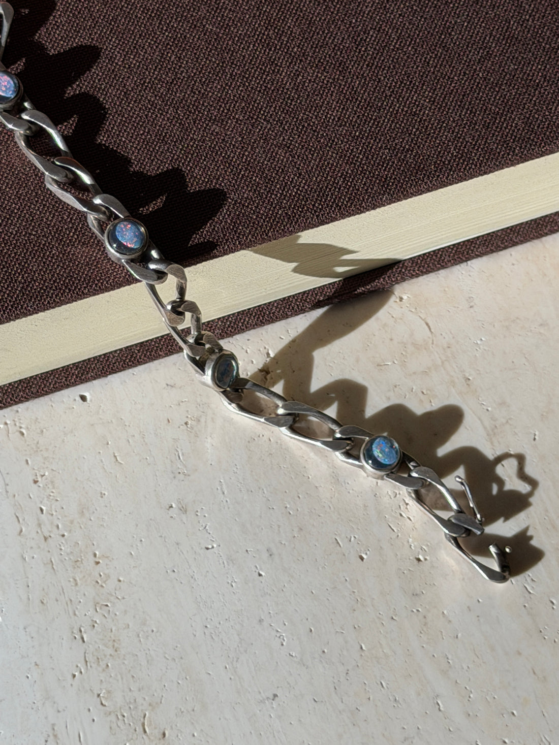 Close view of the opal bracelet over a book edge, red and blue fire flickering in the round cabochons beside the box clasp