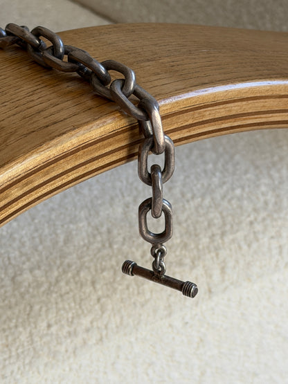 Bracelet draped over the curved edge of a wooden chair arm, showing the toggle T-bar clasp in detail