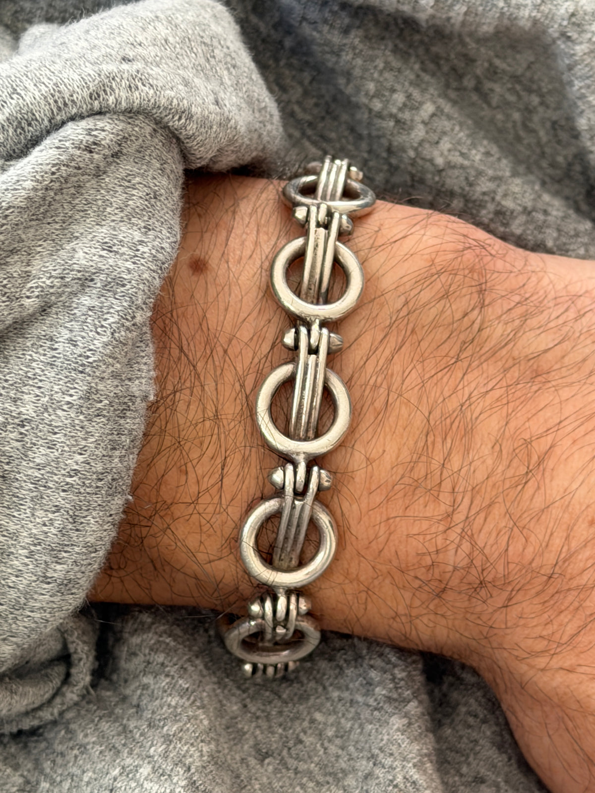 Close wrist view of the ring and bar link bracelet, the satin silver rings and ribbed bar bundles with small rivet like studs