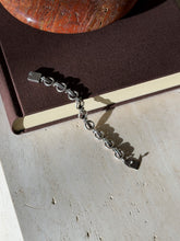 Ring and bar link bracelet draped from a brown book onto travertine, its flat hinged tab clasp at each end