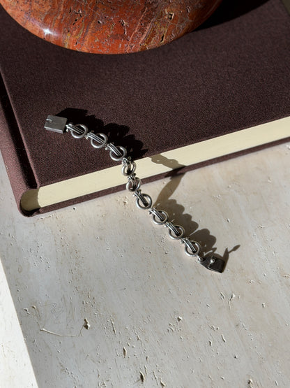Ring and bar link bracelet draped from a brown book onto travertine, its flat hinged tab clasp at each end