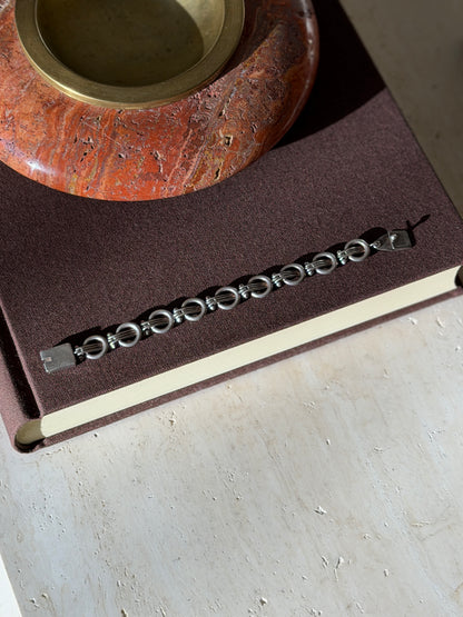 Overhead view of the sterling ring and bar bracelet laid straight on a brown book beneath a red stone ashtray with brass well