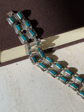 Wide sterling and turquoise panel bracelet draped from a brown book onto travertine, casting stepped shadows in sunlight
