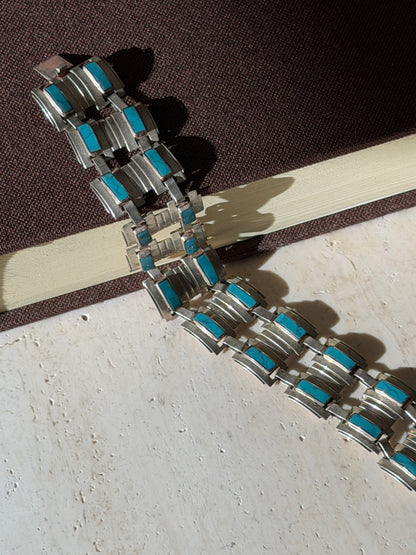 Wide sterling and turquoise panel bracelet draped from a brown book onto travertine, casting stepped shadows in sunlight