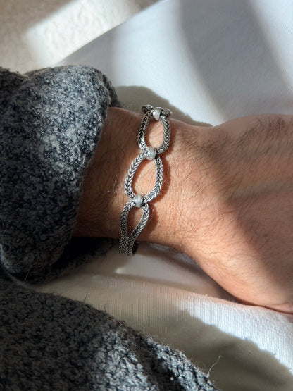 Braided loop bracelet on the wrist in strong sunlight, the herringbone weave of each oval and the matte sleeve connectors in sharp relief
