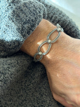 Rope twisted loop bracelet worn over a gray knit cuff, light catching the oxidized grooves of the braided silver links