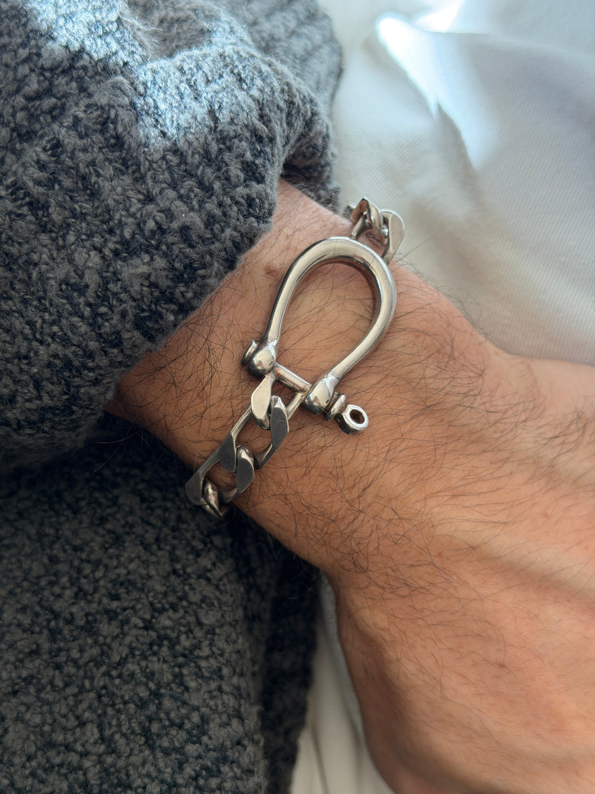 Close view of the silver horseshoe shackle on the wrist, its smooth curved bow, ball shoulders, and threaded crossbar pin
