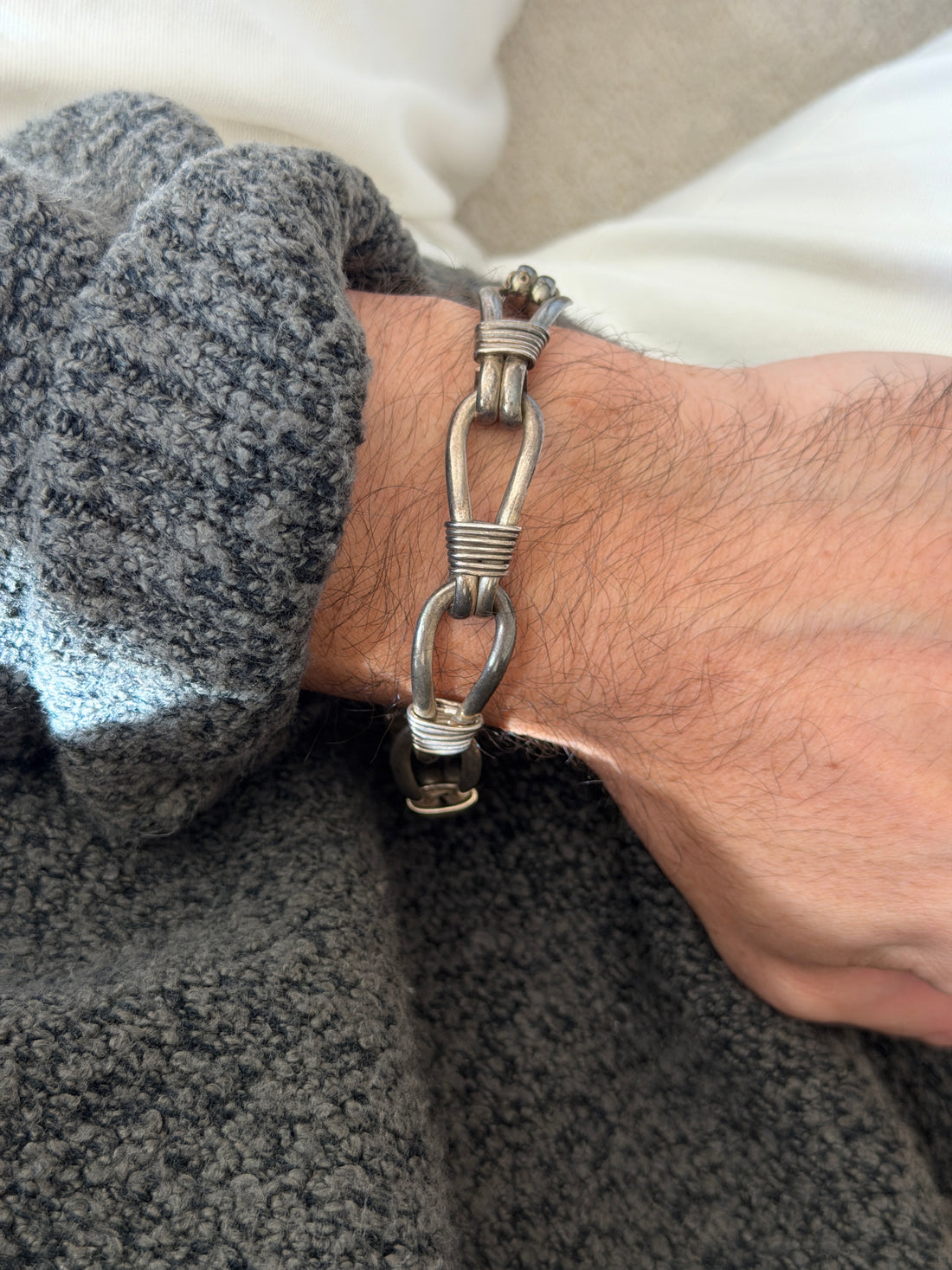 Vintage sterling silver nautical rope link bracelet of elongated teardrop loops bound with coiled wire wraps, worn on the wrist against a gray knit cuff