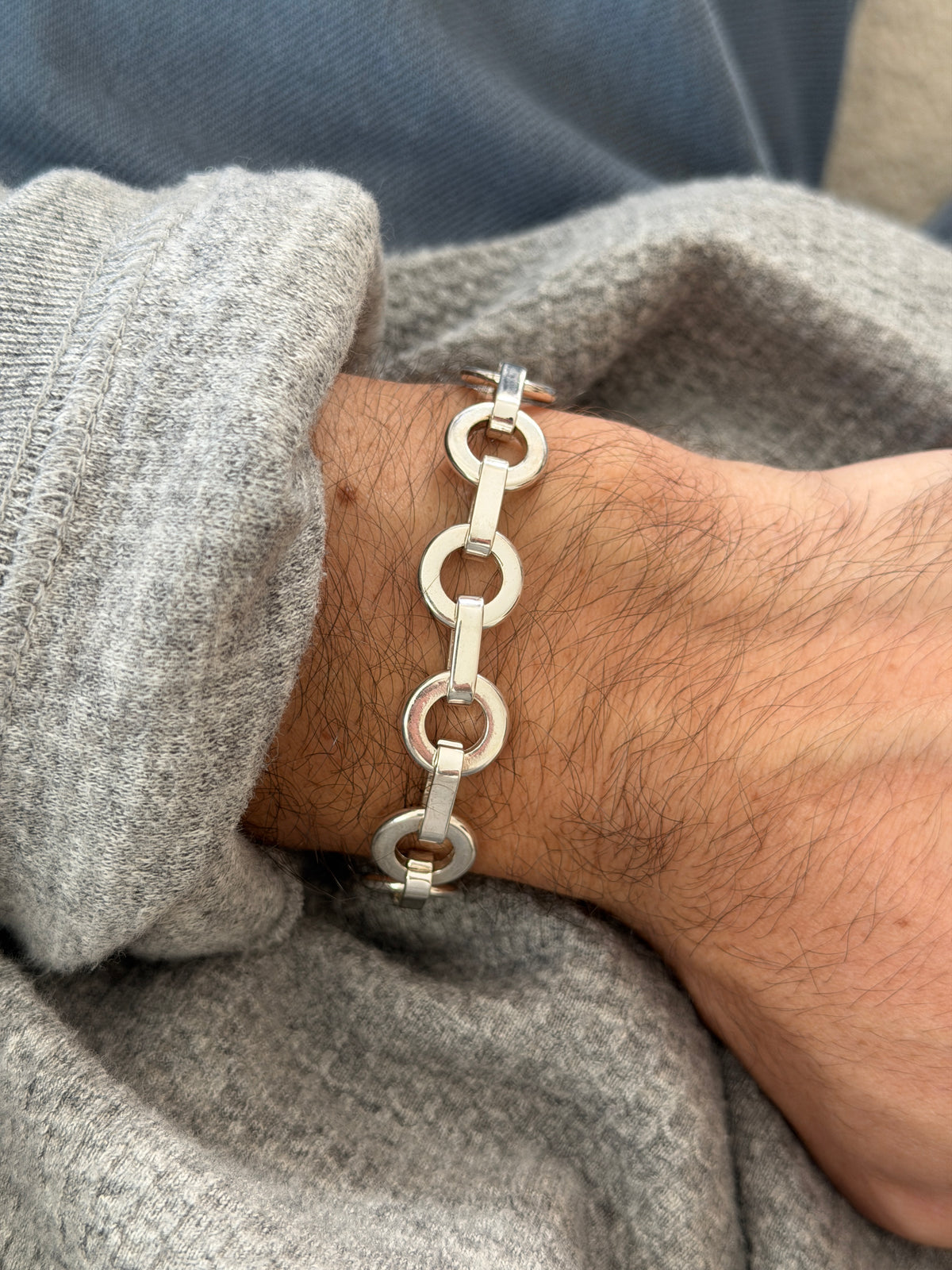Vintage sterling silver bracelet of flat round rings joined by polished bar links, worn on the wrist over a gray sweater