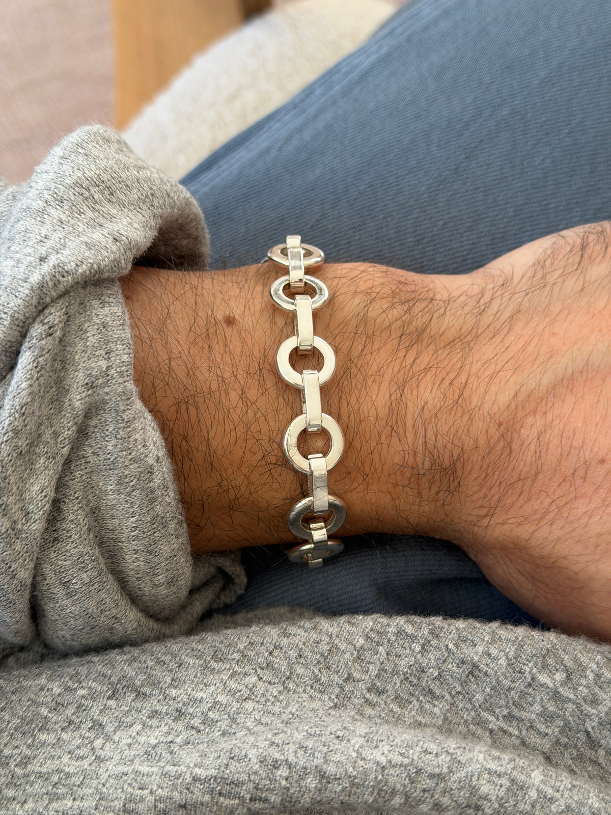 Round link silver bracelet on the wrist against blue denim, the polished rings catching soft daylight