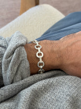 Round link bracelet worn on the wrist beside a cream boucle chair arm, the chain of rings and bars in profile