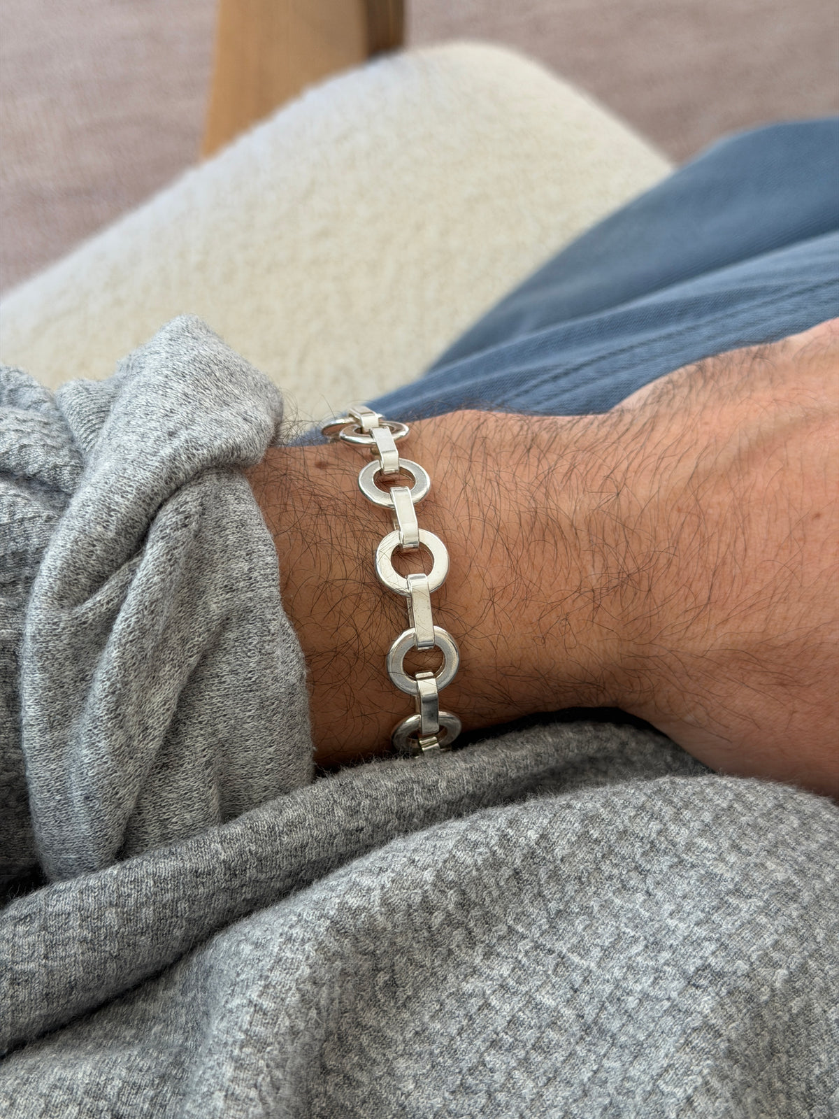 Round link bracelet worn on the wrist beside a cream boucle chair arm, the chain of rings and bars in profile