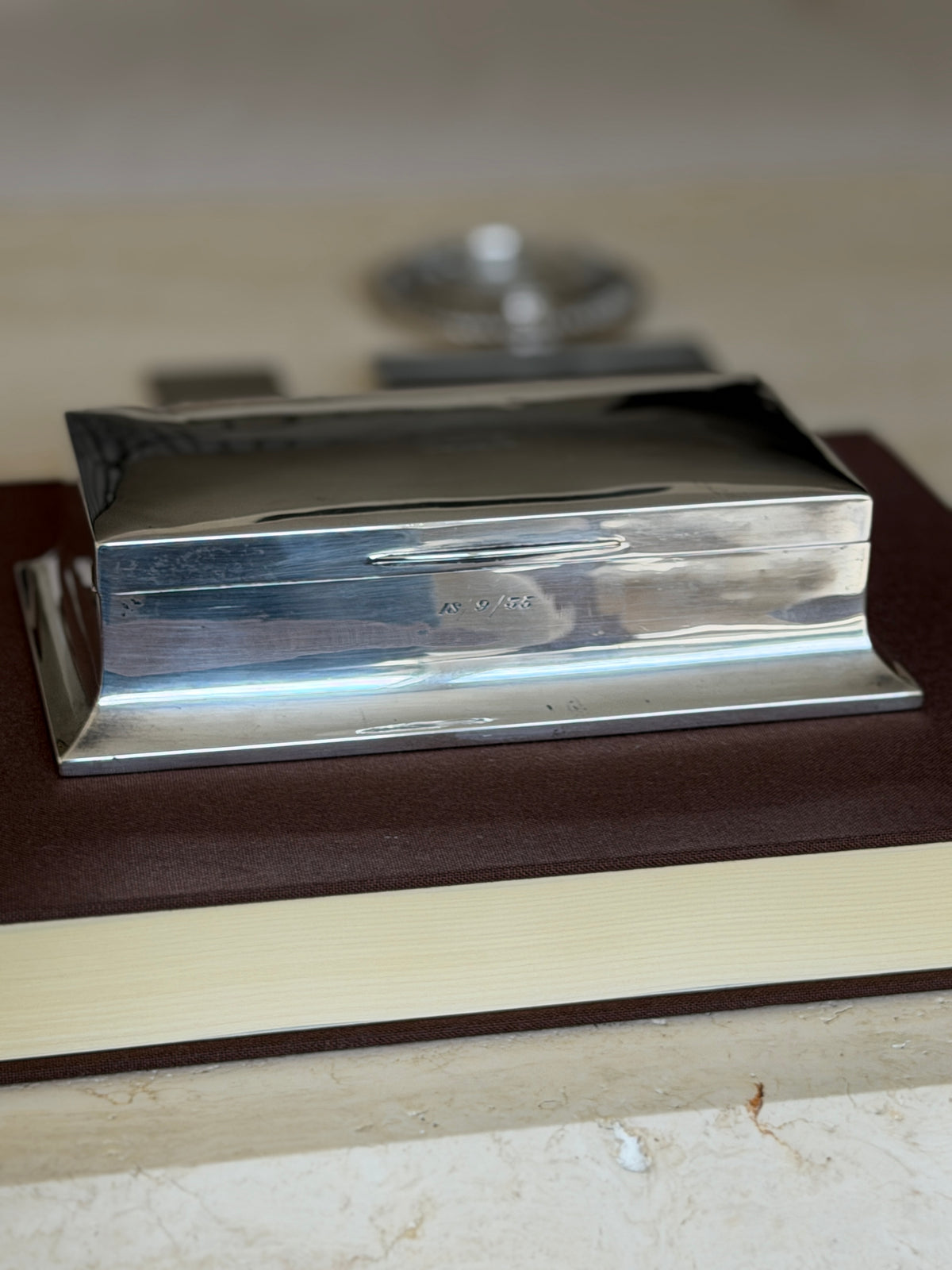 Eye level side view of the sterling box showing the flared stepped base, slim thumb lip, and engraved date 15/9/55