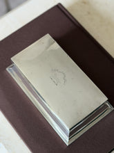 Overhead view of the box lid with a leaping cat crest above a twisted wreath and a scrolling motto ribbon