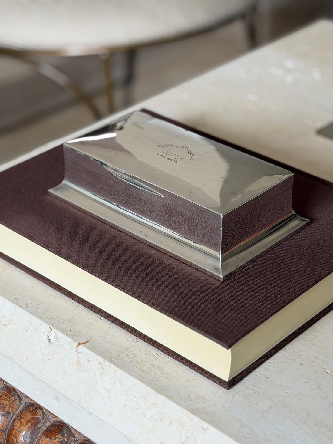 Angled view of the Walker and Hall box on a brown book, the hinged lid and splayed rectangular base in daylight